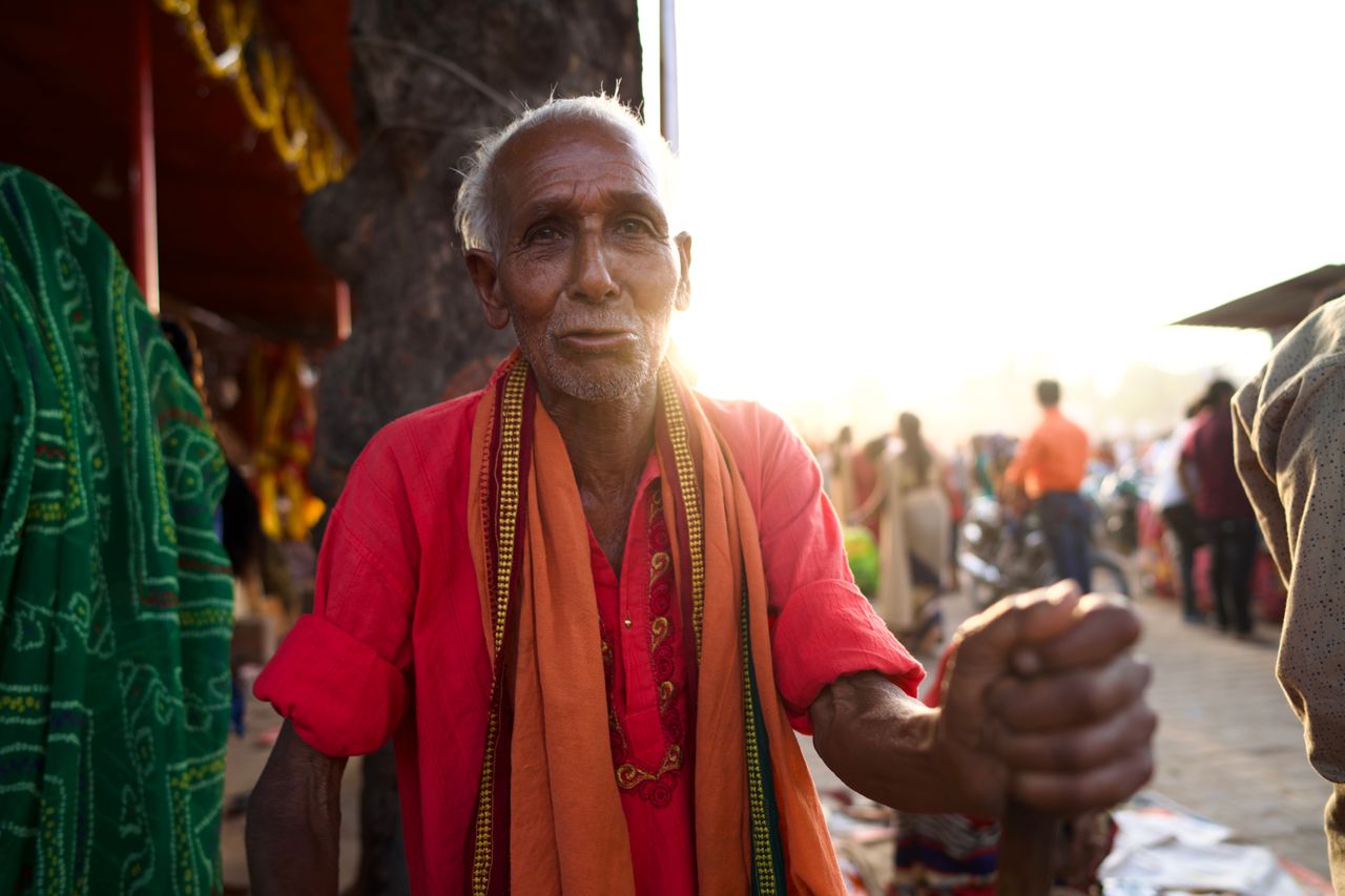 Portrait of an elderly man in vibrant traditional clothing in an outdoor urban setting at sunset.